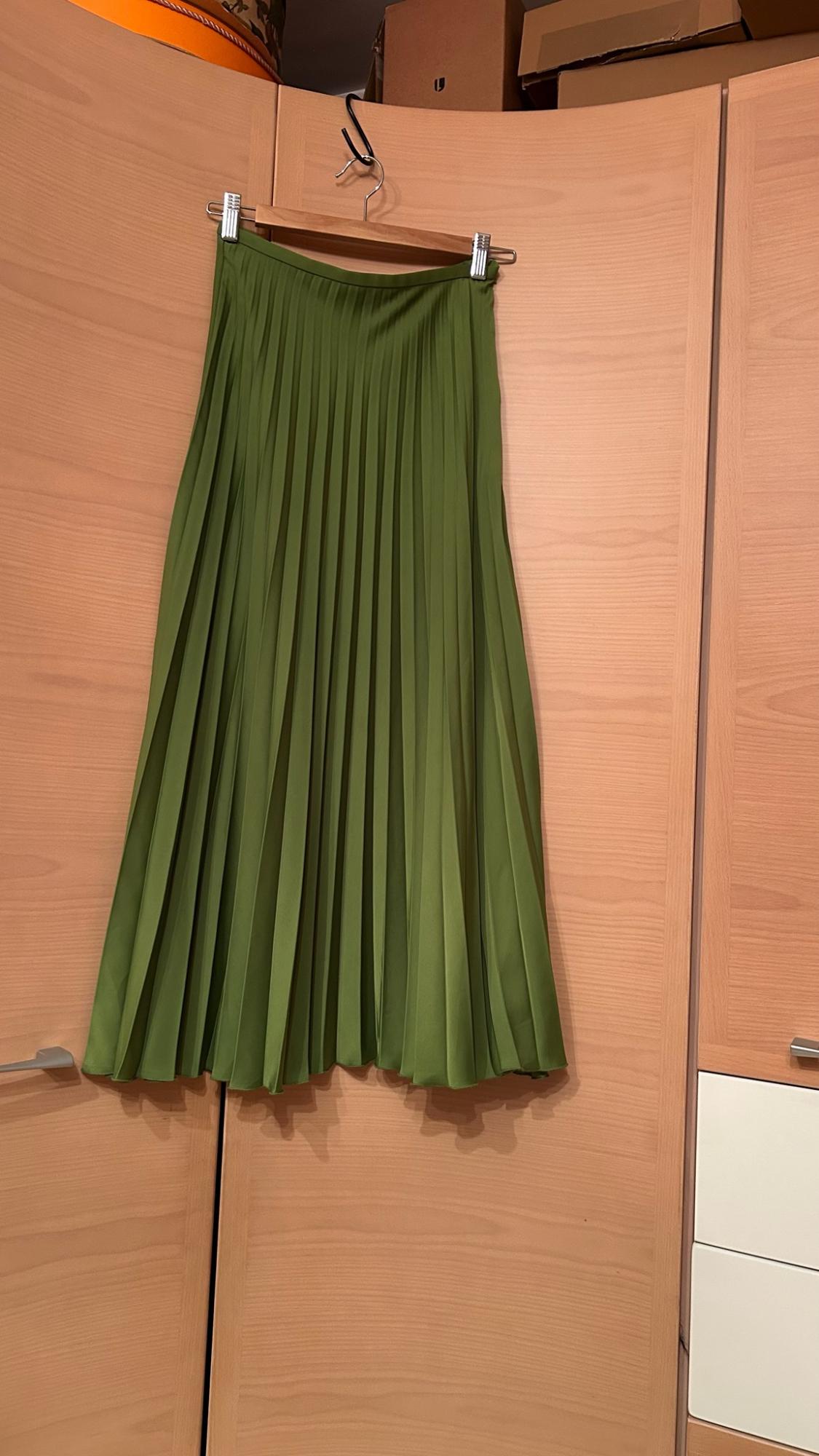 Green pleated skirt hanging on a wooden hanger on the doors of a light-coloured wardrobe, in a relaxed and casual setting.