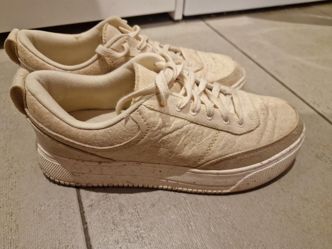 Beige trainers on grey wooden floor. Simple design with laces and textured white sole.