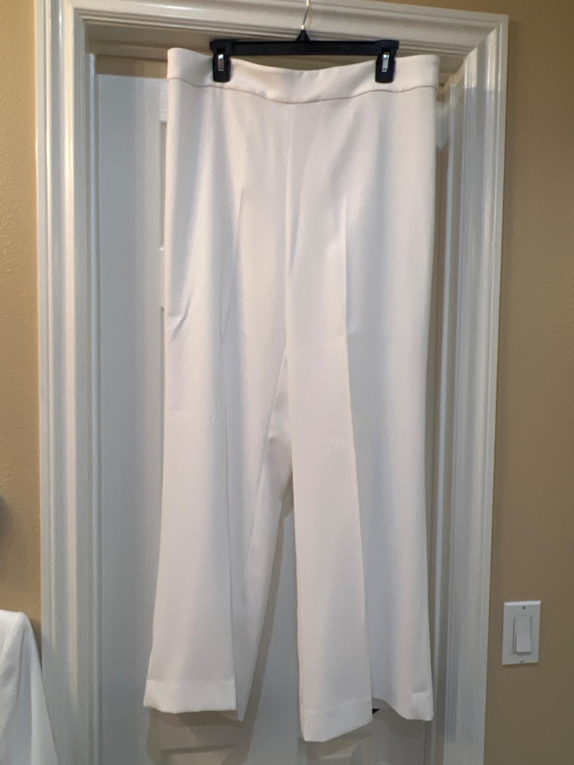 White trousers hanging on a black hanger over a white door, with light beige walls around.