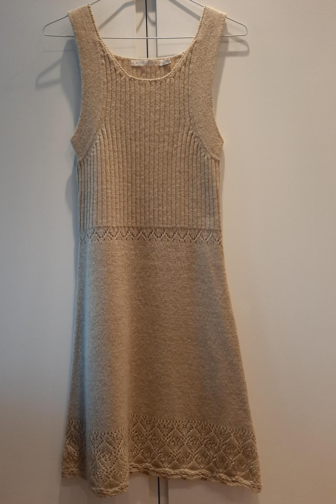 Front view of a sleeveless beige dress with a knitted trim and a cut-out detail at the hem.