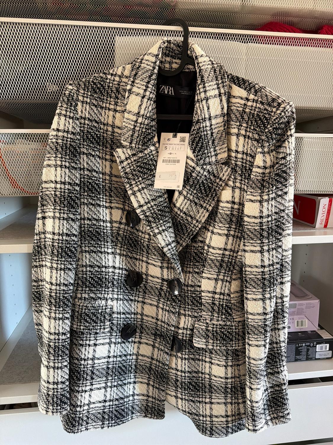 Black and white checked blazer hanging up. Texts: ZARA, S, 79 on label; REVLON, WHAT MAKES IT SPECIAL on box.
