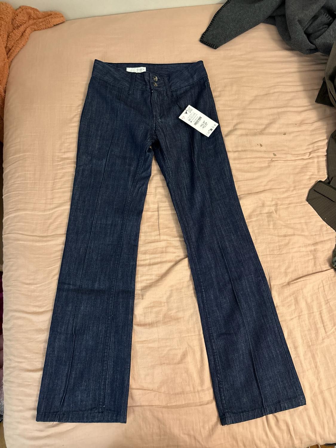 Dark blue flared denim trousers with front seams, on a beige sheet. They have a label at the waist.