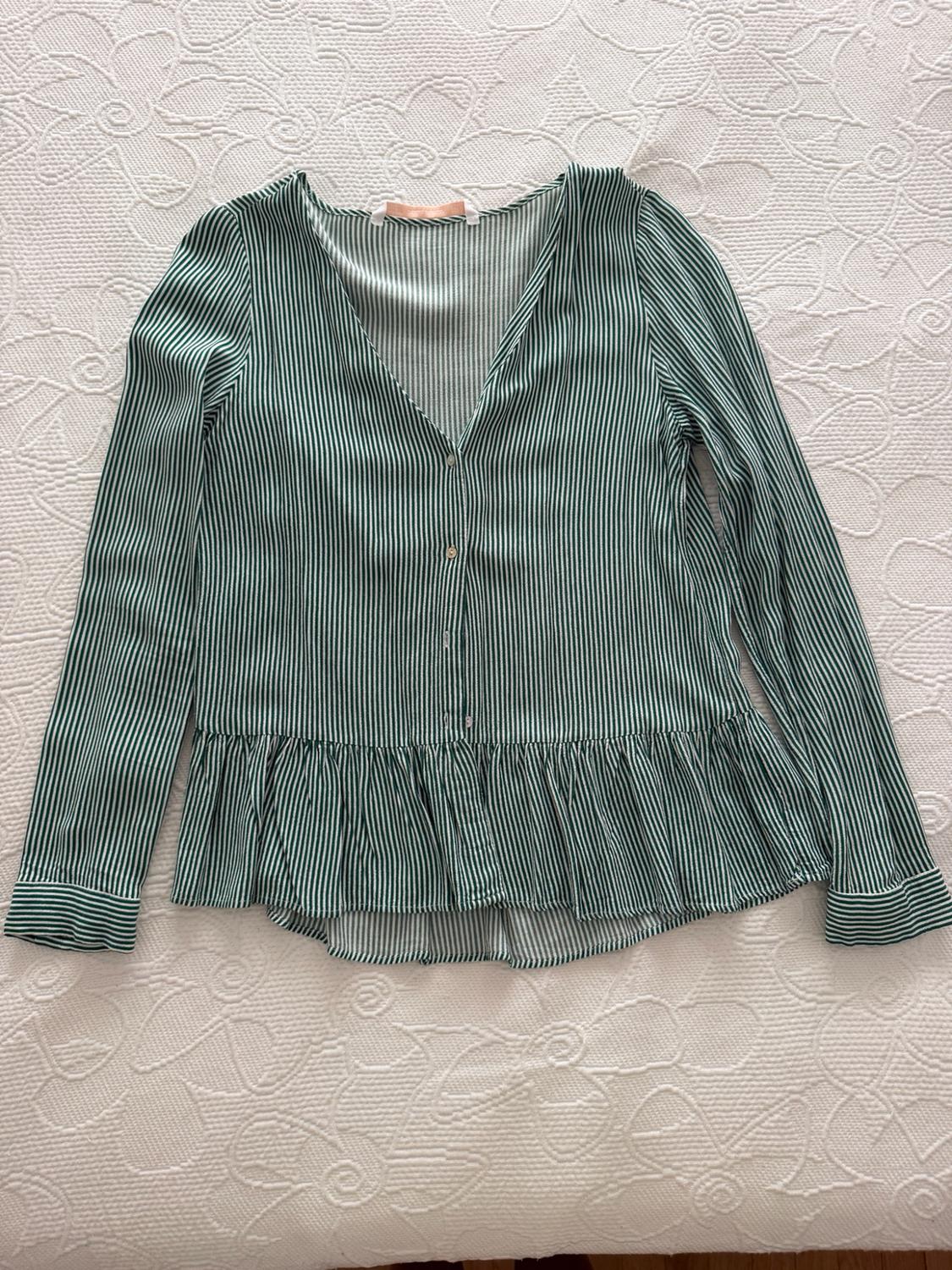 Green and white vertical striped blouse with a V-neck, front buttons and a frilled hem, laid out on a white bedspread.