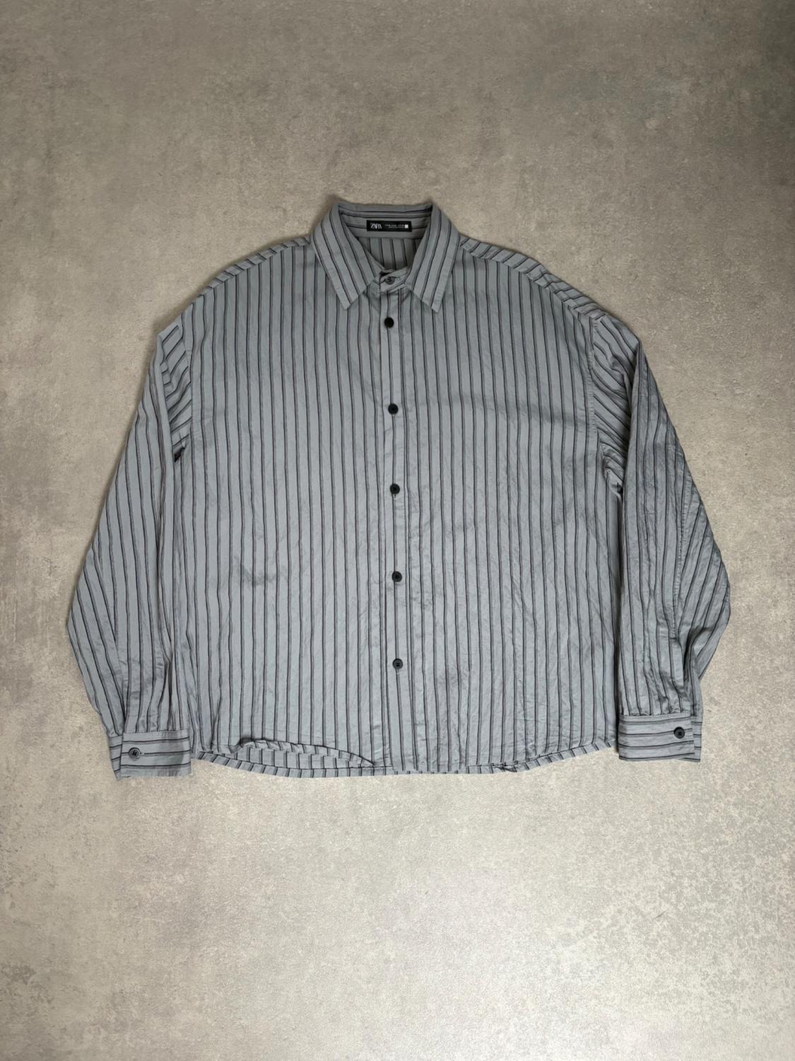 Loose-fitting long-sleeved grey shirt with black vertical stripes and buttons, on a textured grey background. ZARA label.