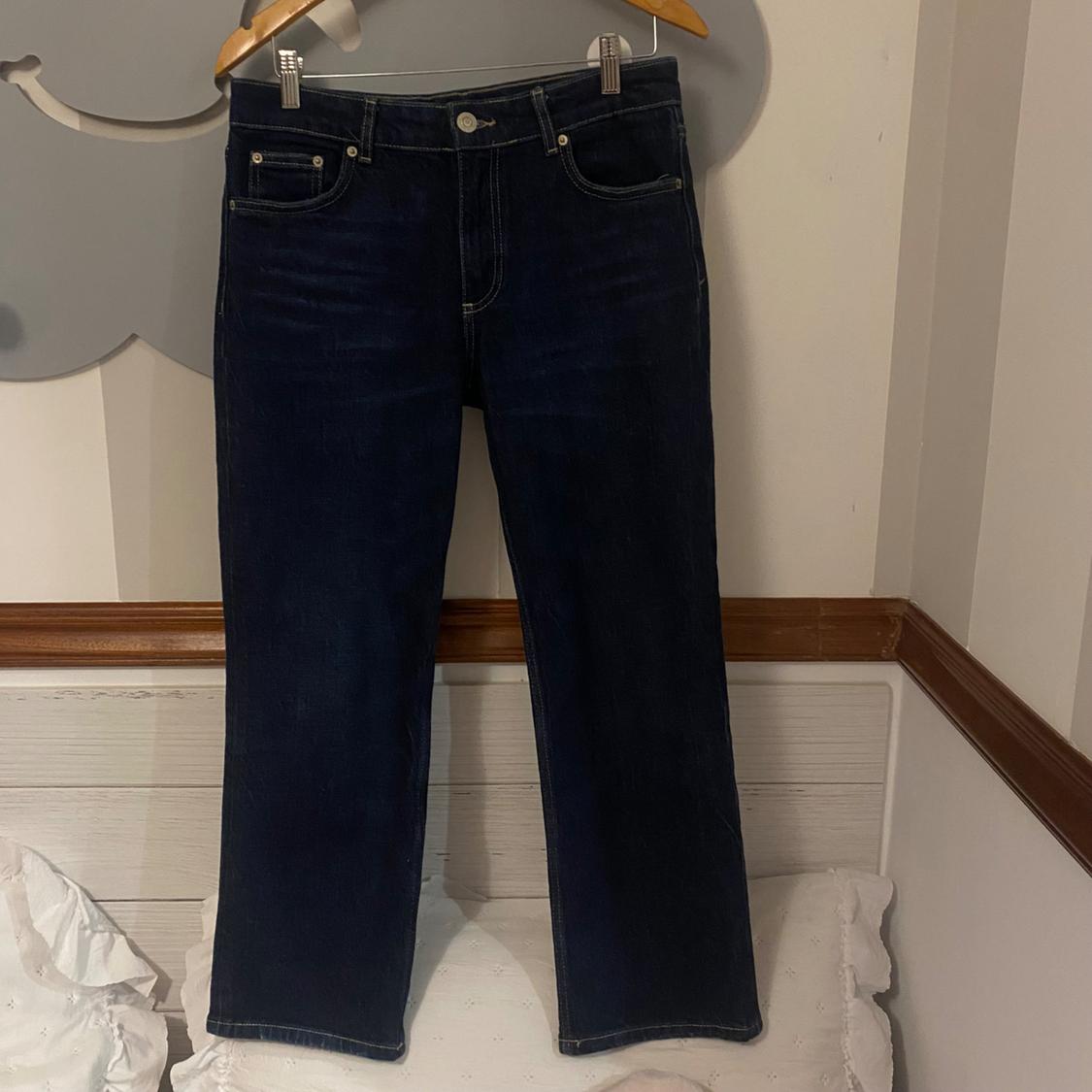 Dark blue jeans hanging on a wooden hanger against a white wall with wooden moulding.