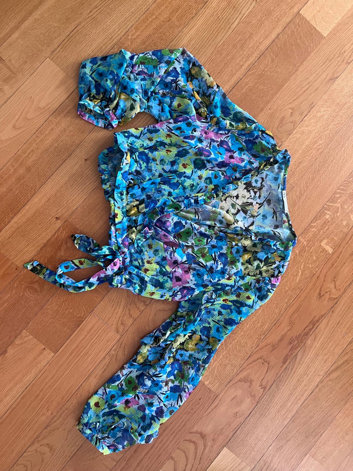 Long-sleeved wrap blouse in a multicoloured floral print in shades of blue and green, with a tie waist, on a wooden floor.