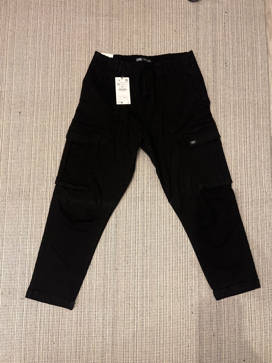 Black cargo trousers with a visible label on a beige fabric background.