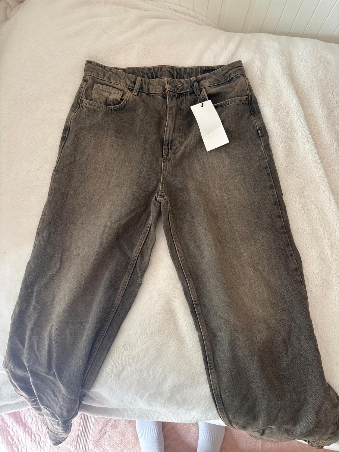 Brown jeans with a white hanging tag, placed on a bed with a white bedspread.
