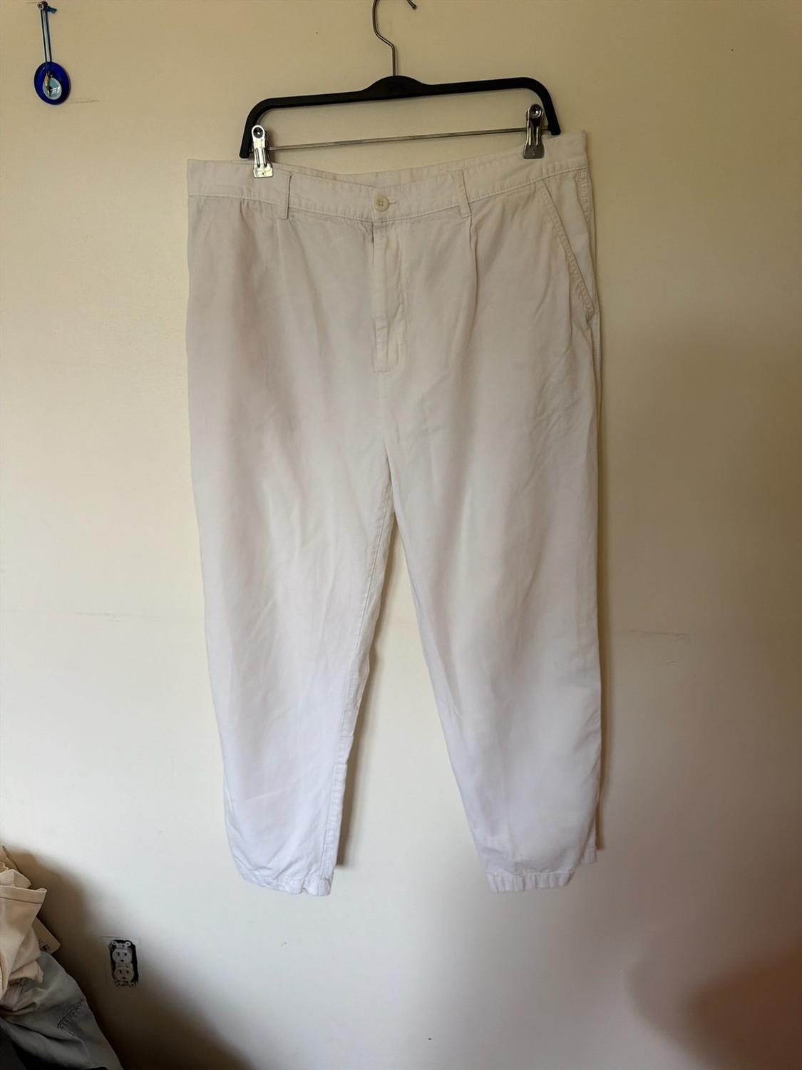 White jogger-style trousers hanging on a black hanger against a light-coloured wall. To the left, there is a blue amulet and a plug socket below.
