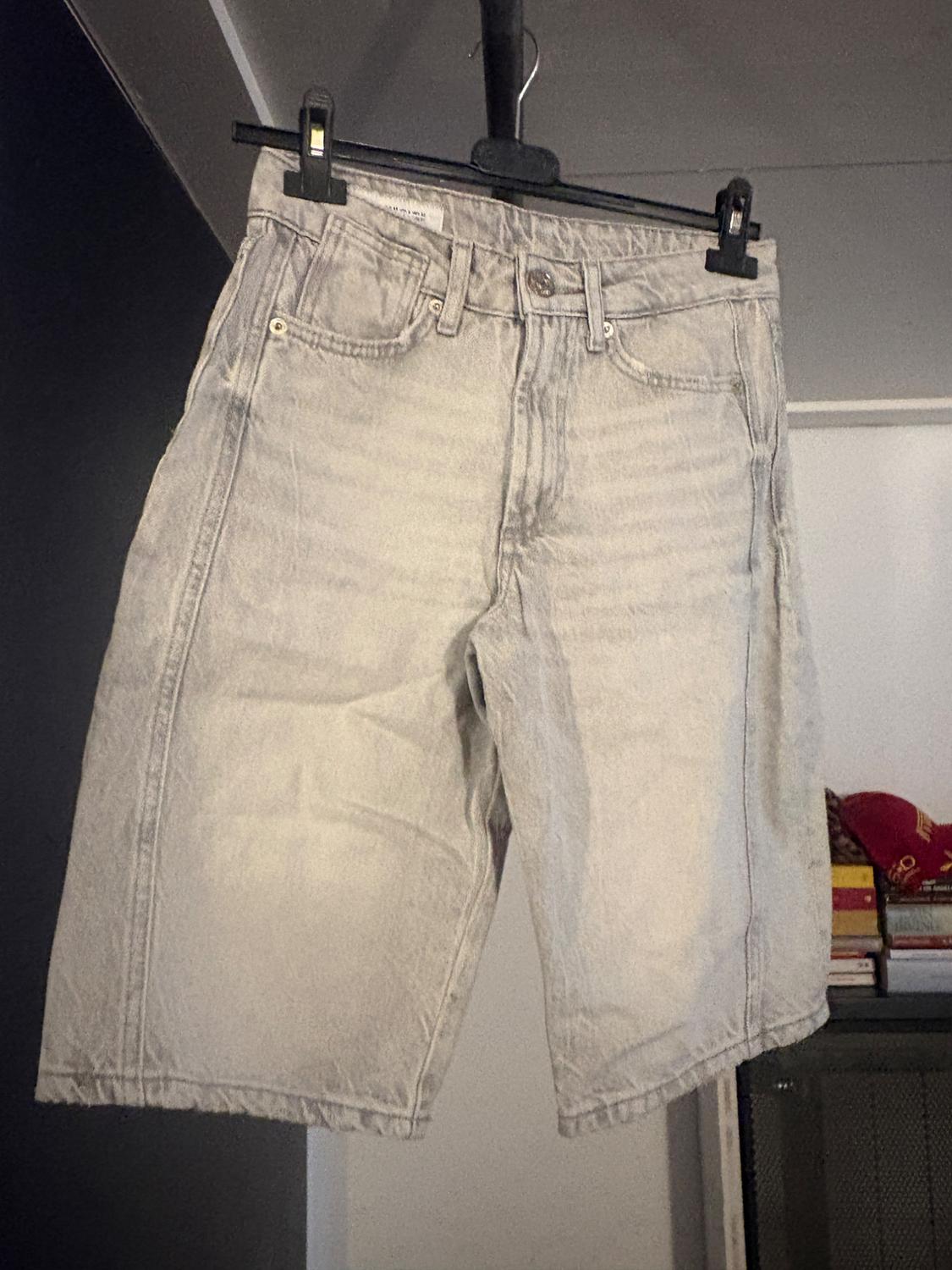 Light grey denim shorts hanging on a black hanger, indoor background with stacked books.