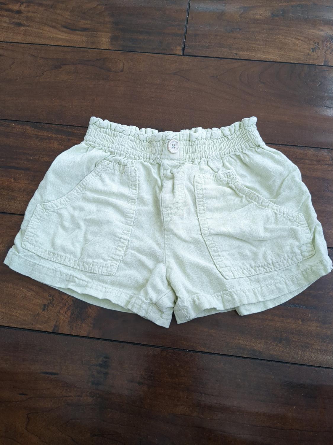 Front view of beige shorts with a gathered elastic waistband and side pockets.