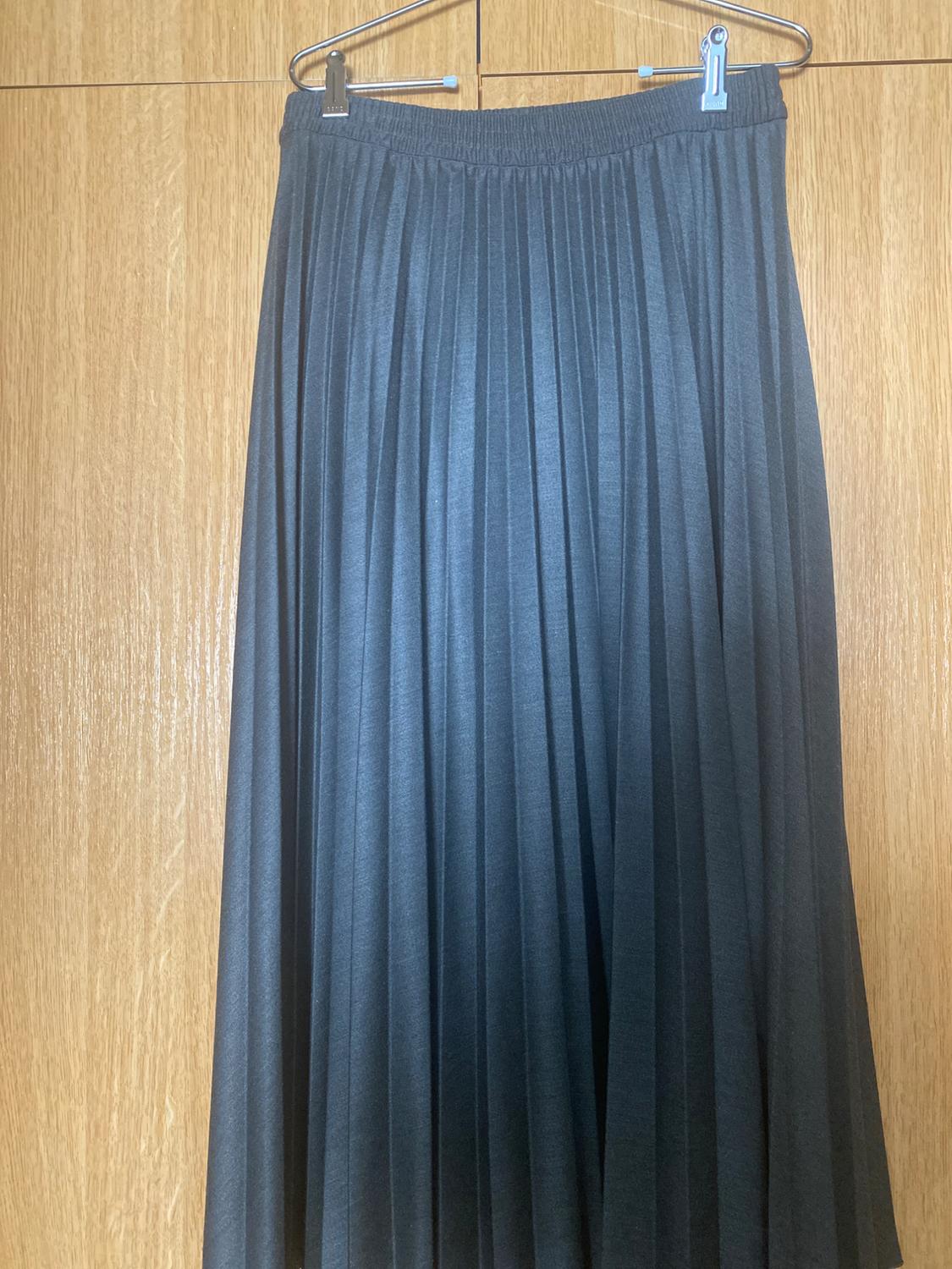 Black pleated skirt hanging on a hanger against a light wooden background.