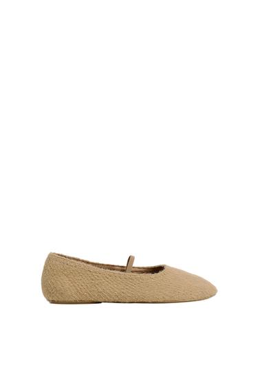 Beige ballerina flat with soft texture and thin strap over the instep, minimalist white background.