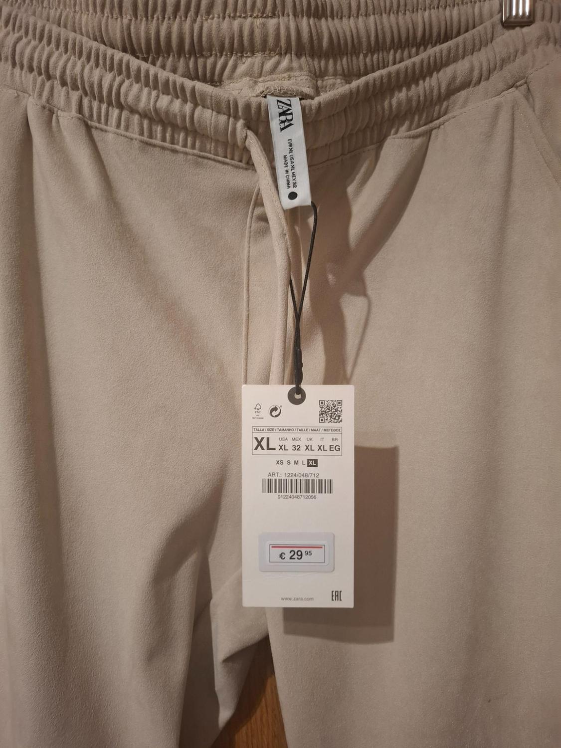 Beige trousers with an elasticated waist and a price tag of €29.95. Size XL visible on the swing tag.