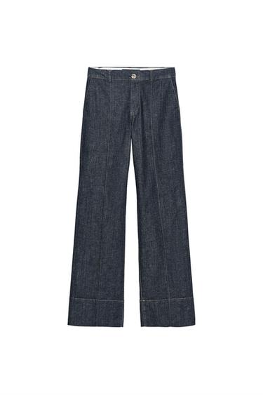 Front view of high-waisted blue trousers with front pleats, front pockets, and zip and button fastening.