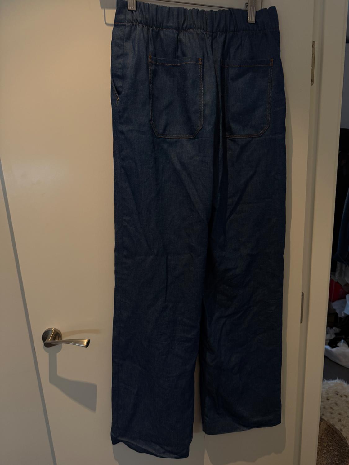 Blue denim trousers hanging on a white door. They have an elasticated waist and visible back pockets.