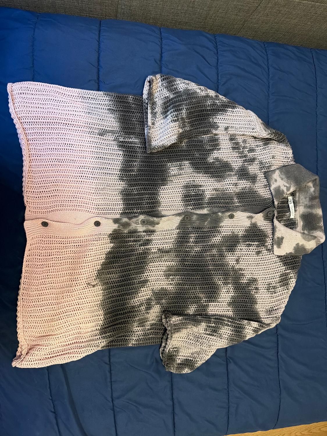 Knitted shirt with a tie-dye effect in pink and grey tones, on a blue bedspread.