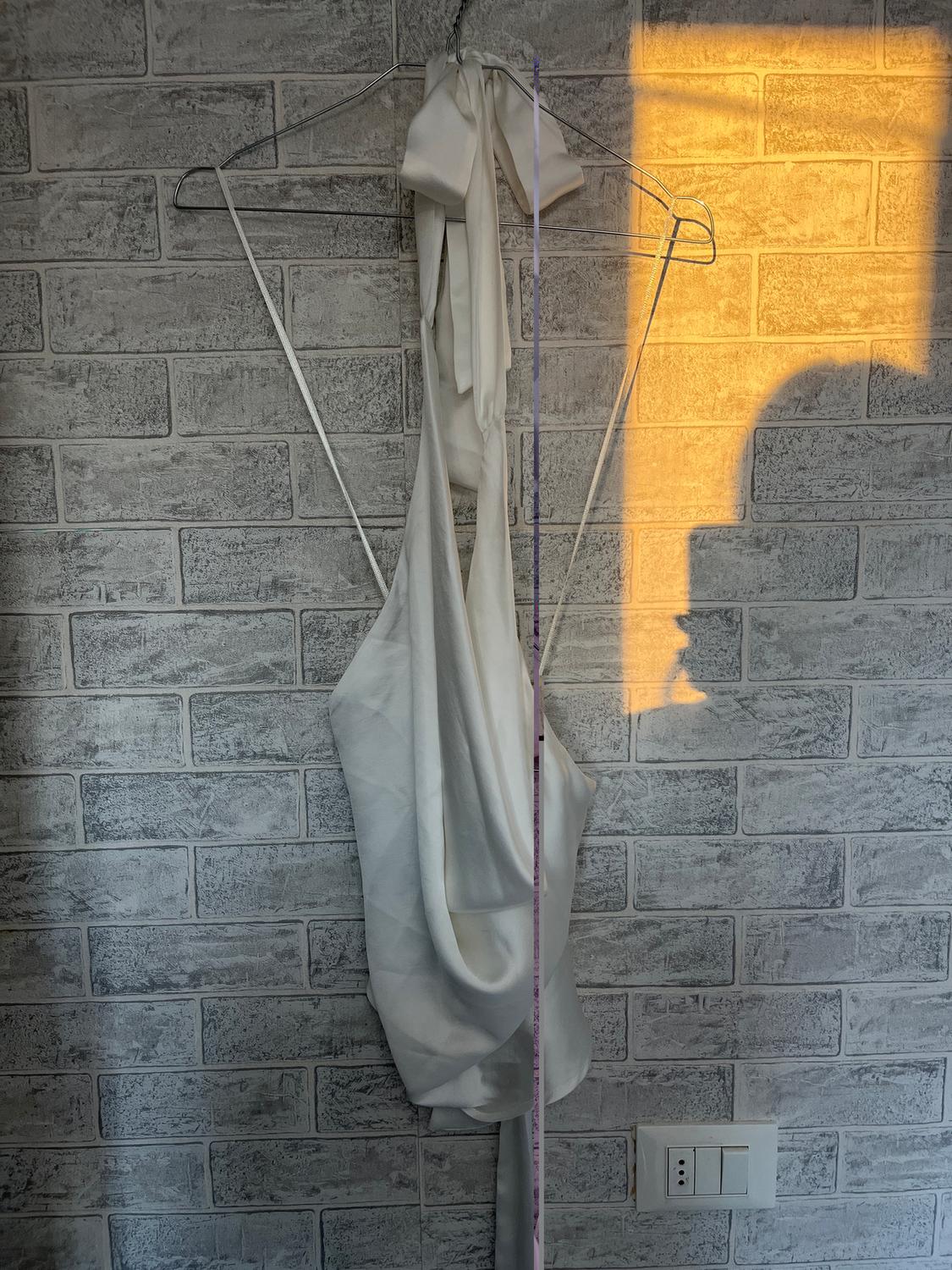 White blouse hanging on a hanger against a grey brick wall, illuminated by warm evening light.