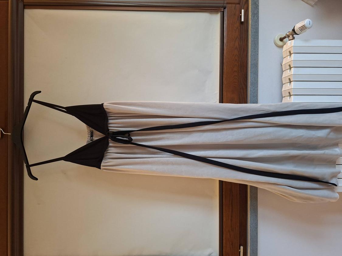Long white dress with black straps hanging on a hanger in front of a wooden window.