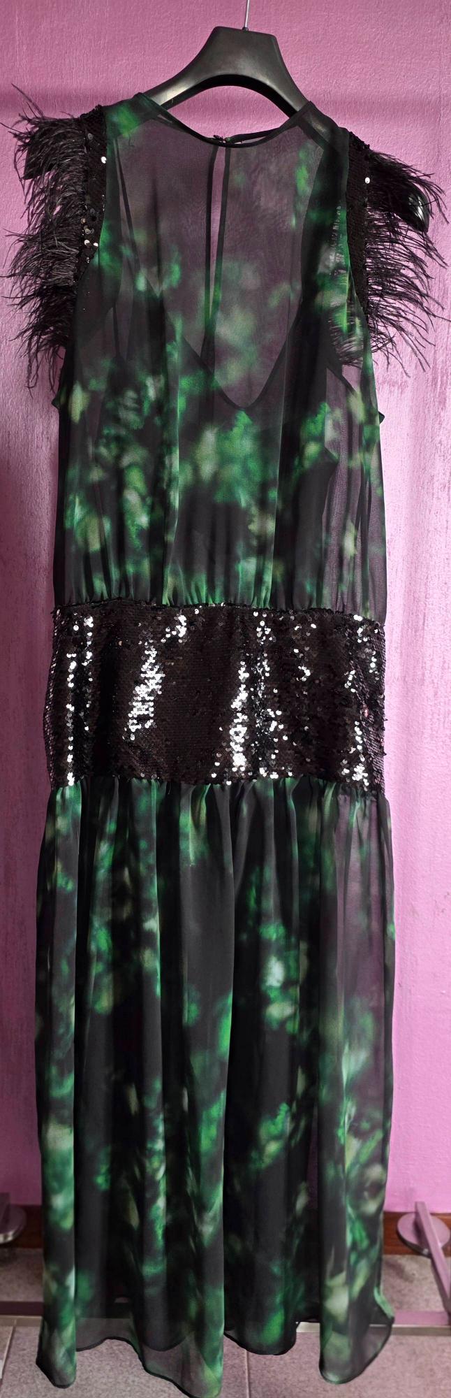 Long hanging dress, with a green and black print, feather details on the shoulders and sequins on the waist, pink background.