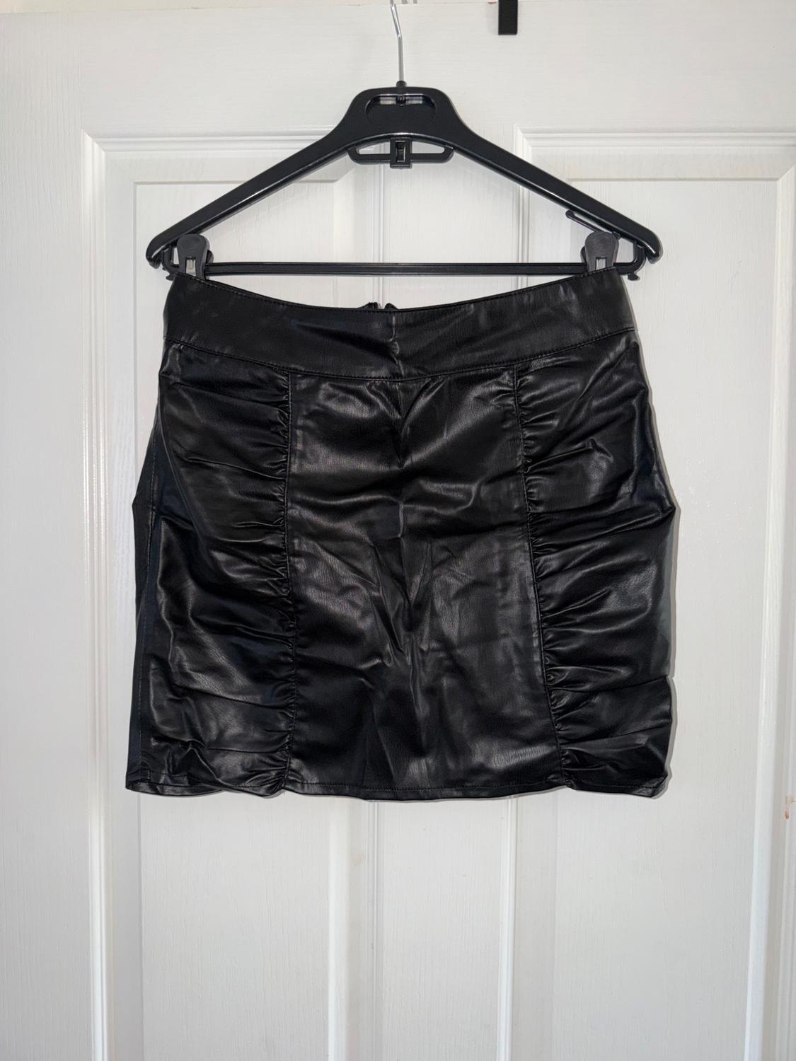 Black synthetic pleated skirt, hanging on a black hanger in front of a white door.