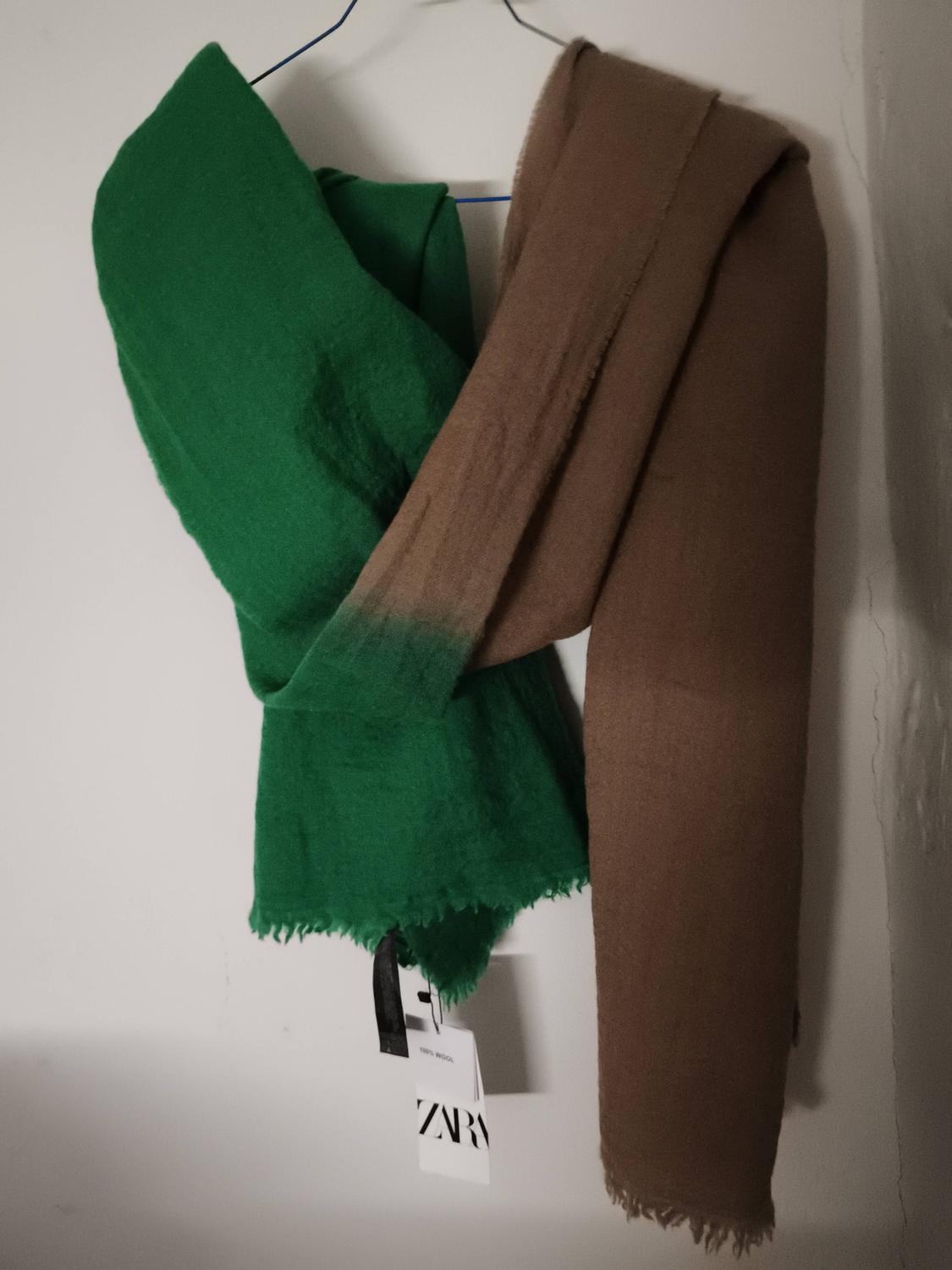 Two-tone scarf, green and brown, hanging on a hanger with visible tags including "ZARA". White background.