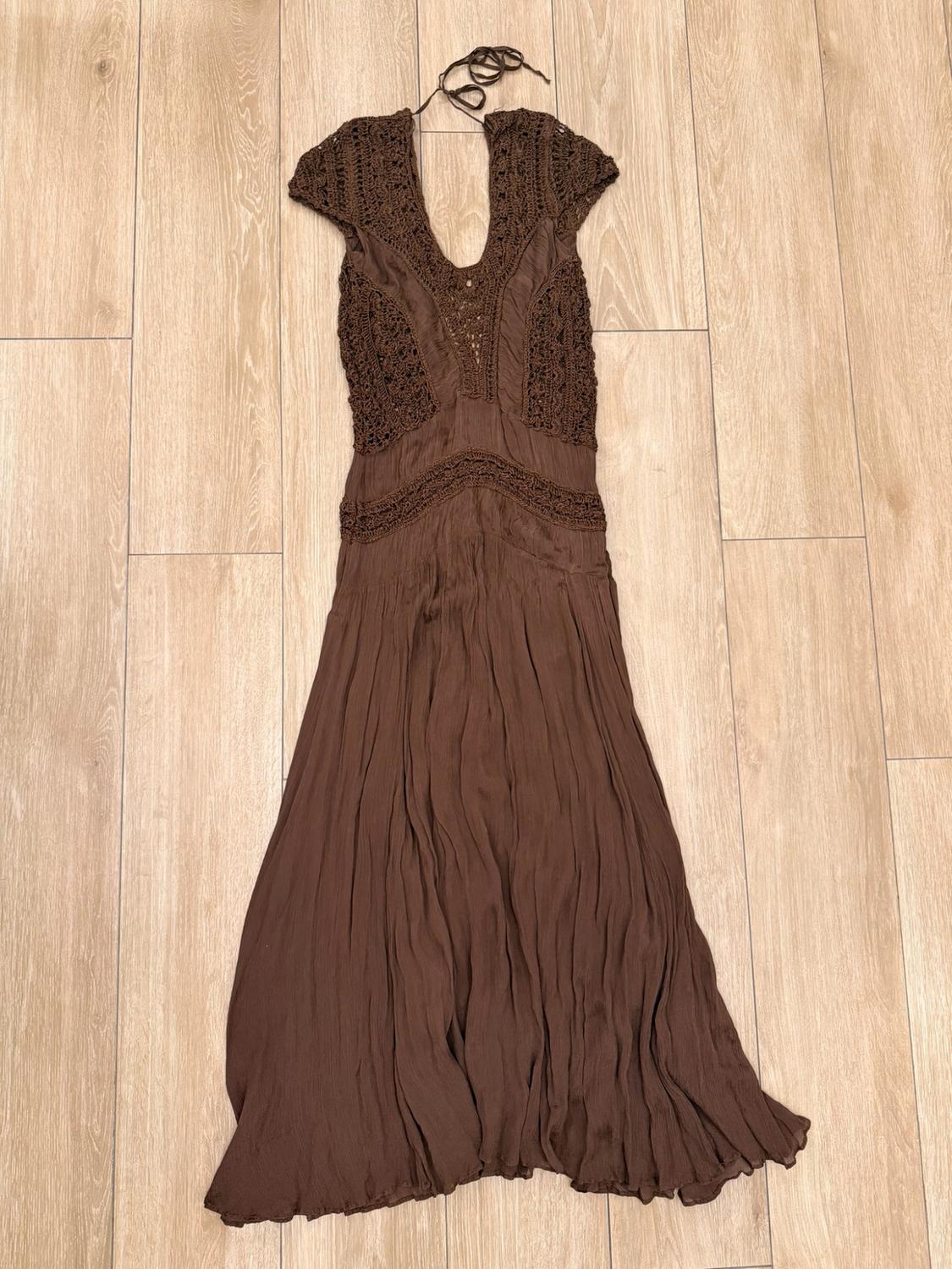 Brown maxi dress with a crochet bodice, V-neckline and a flowing skirt, laid out on a light wood floor.