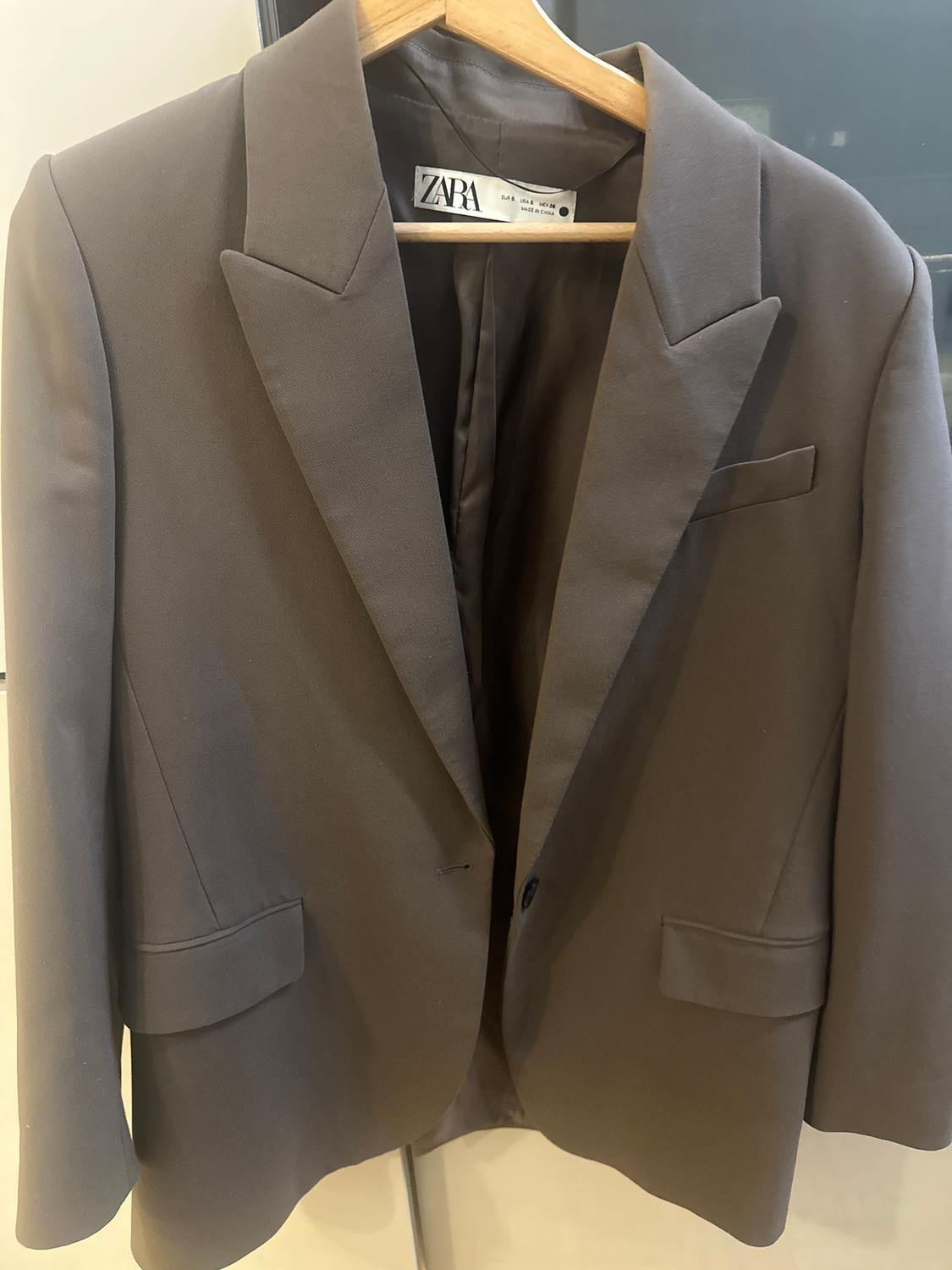 Brown suit jacket hanging on a wooden hanger, with classic lapels and a visible Zara label inside.