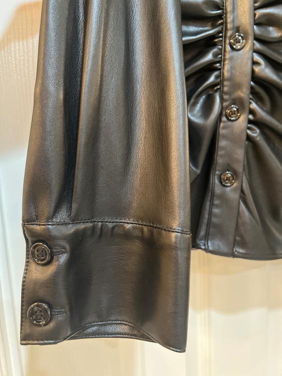 Detail of a black blouse sleeve with shiny buttons and ruching on the body, on a light background.