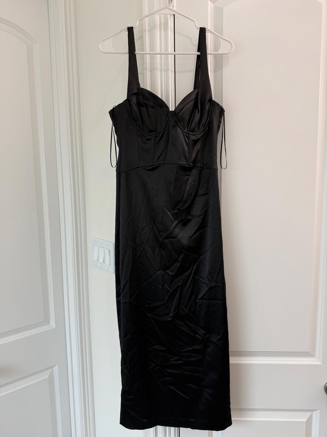 Black spaghetti strap dress hanging on a white hanger over a white door. Satin fabric with visible seams.