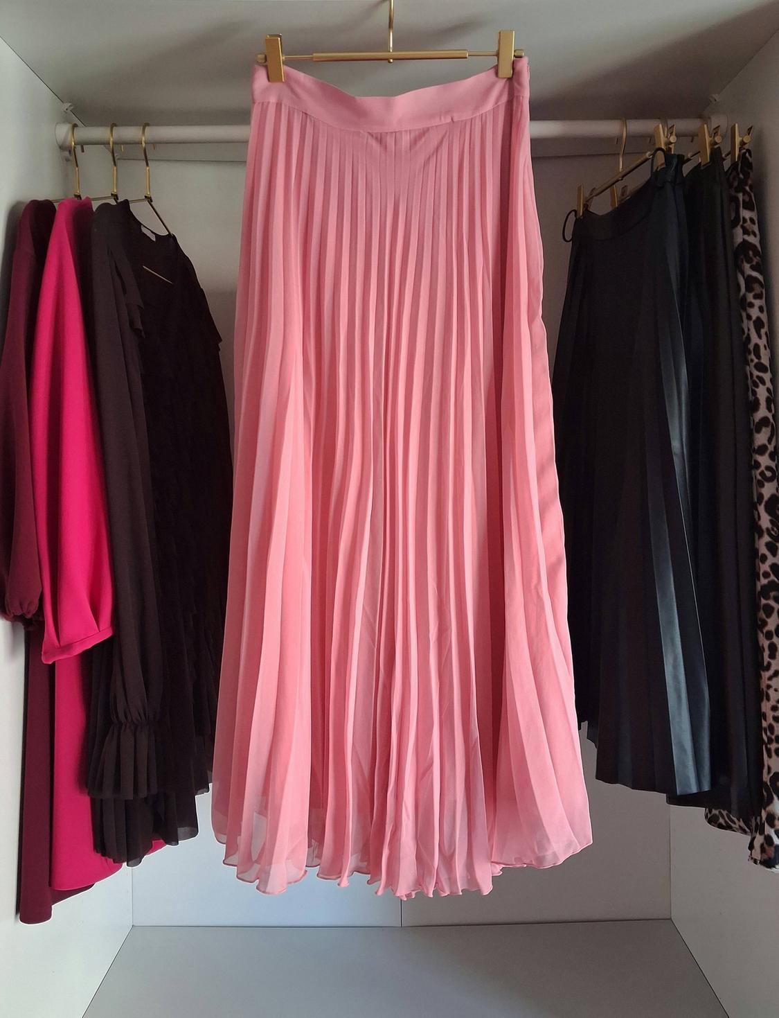 Pink pleated skirt hanging in a wardrobe next to other dark-coloured and leopard print garments.
