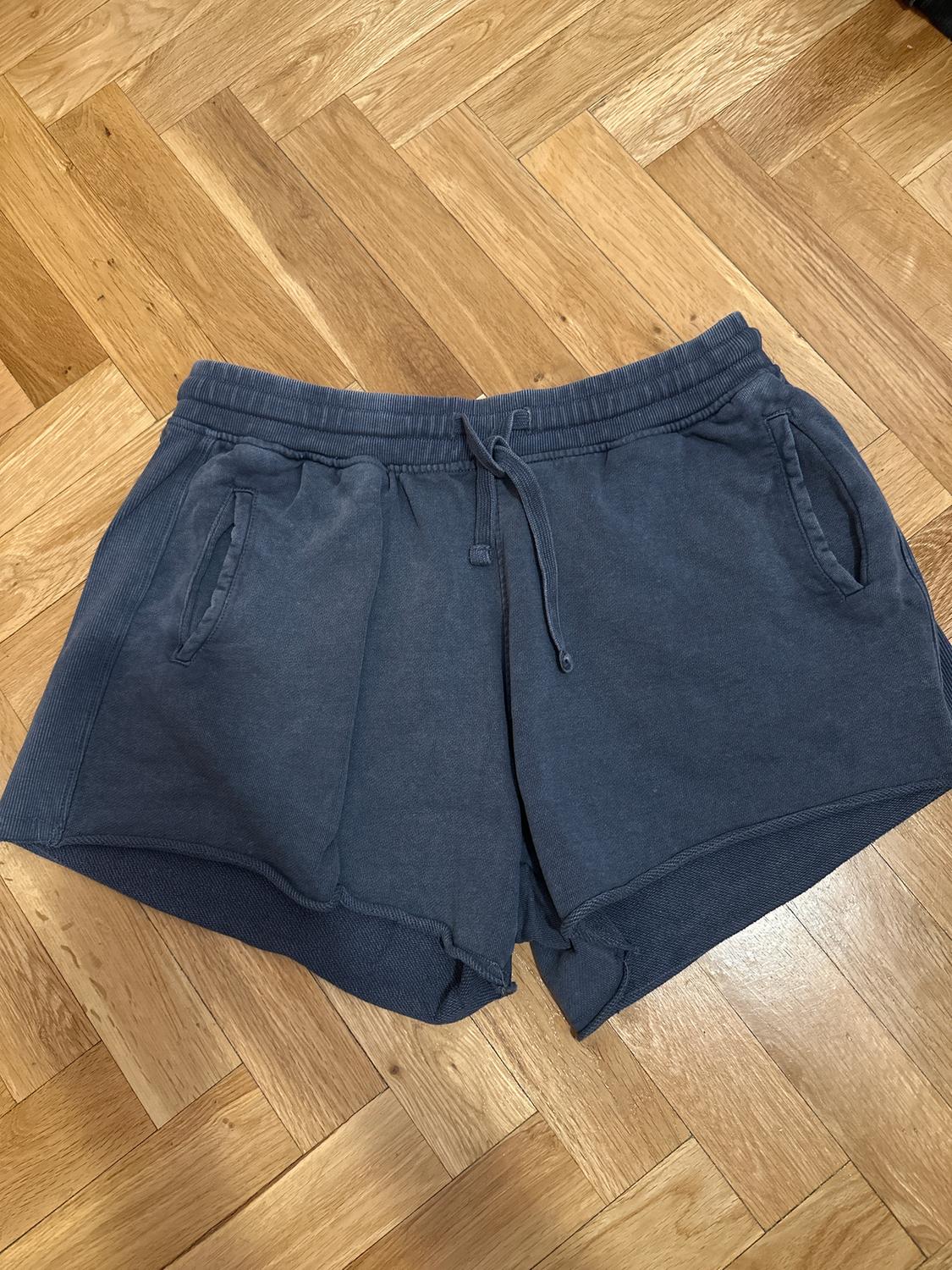 Dark blue shorts with a drawstring and side pockets, on a light herringbone wooden floor.