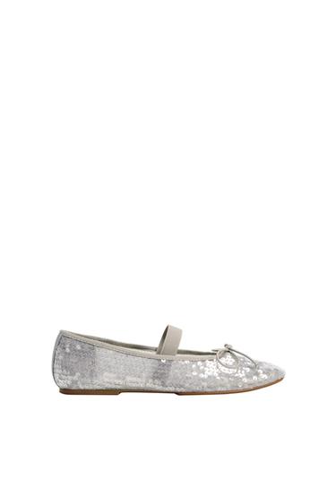 Silver sequinned ballerina pump with a grey elastic strap across the instep and a small bow on the toe, photographed against a white background.
