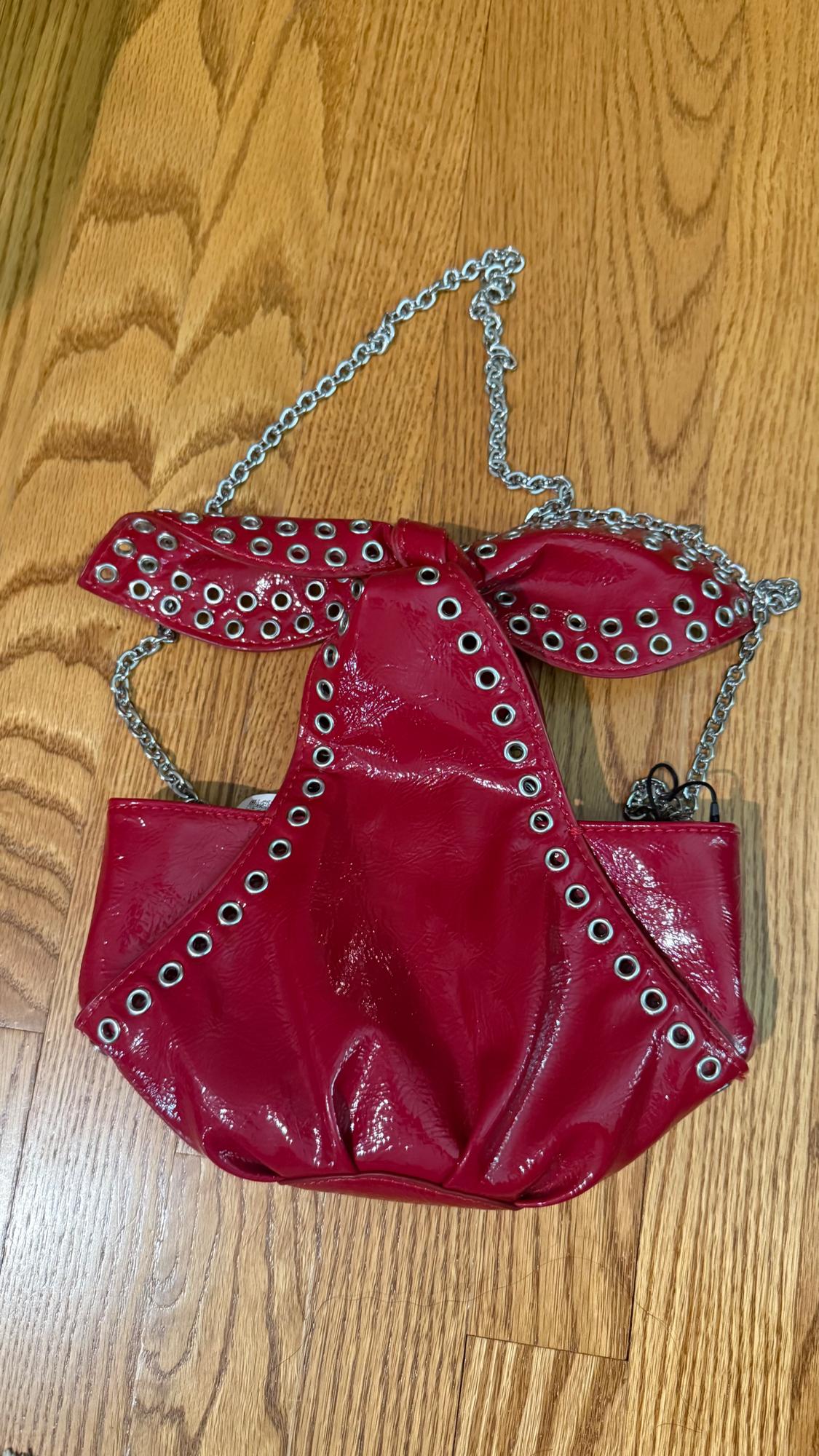 Bright red bag with metal eyelets and silver chain on a light wood floor.