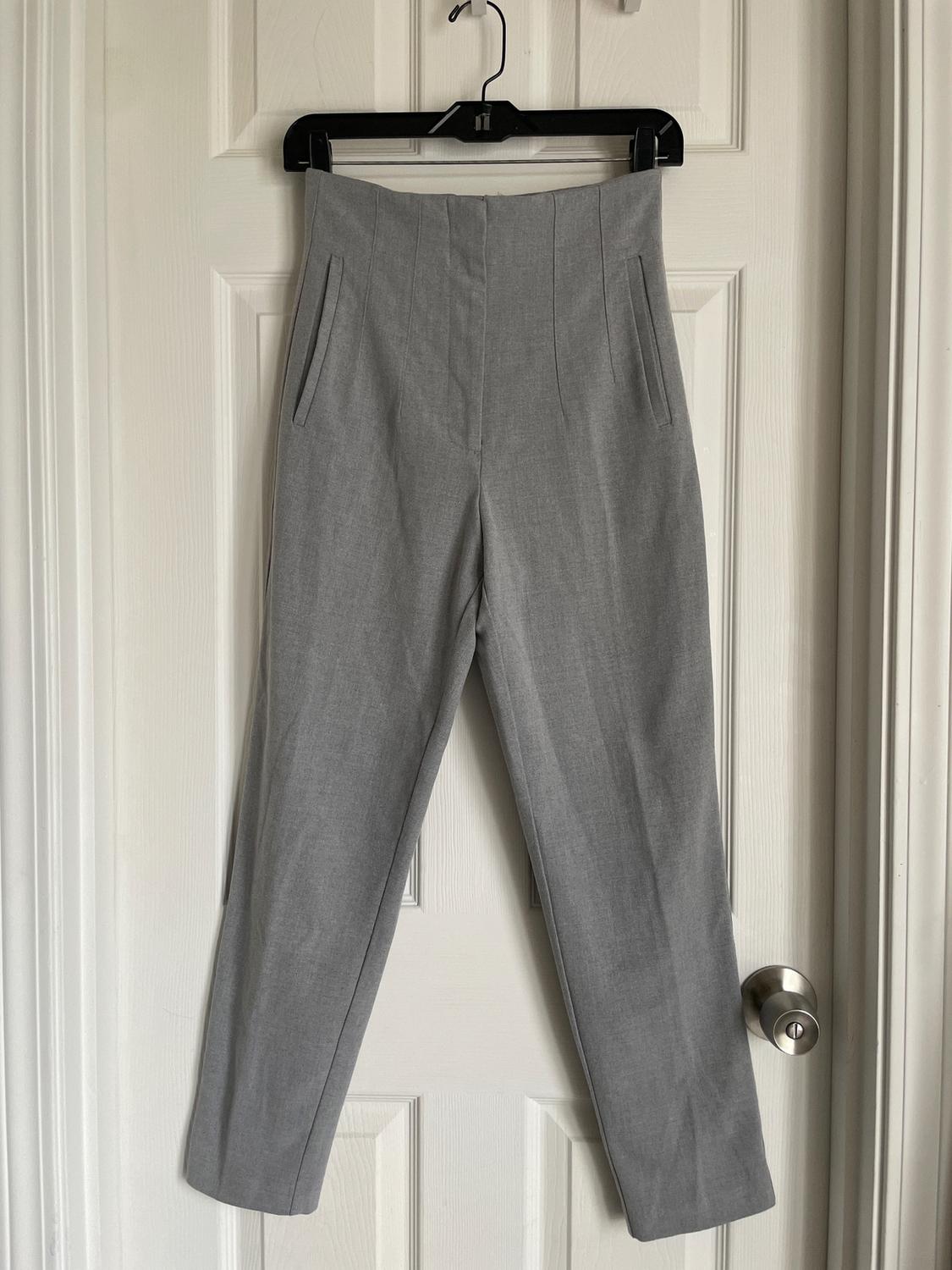 Grey trousers hanging on a black hanger over a white door. Simple design with side pockets.