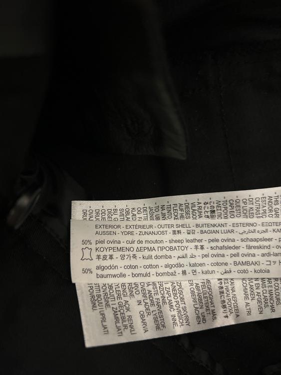 Close-up of a clothing label with multi-language text. States 50% sheepskin and 50% cotton. Dark background.