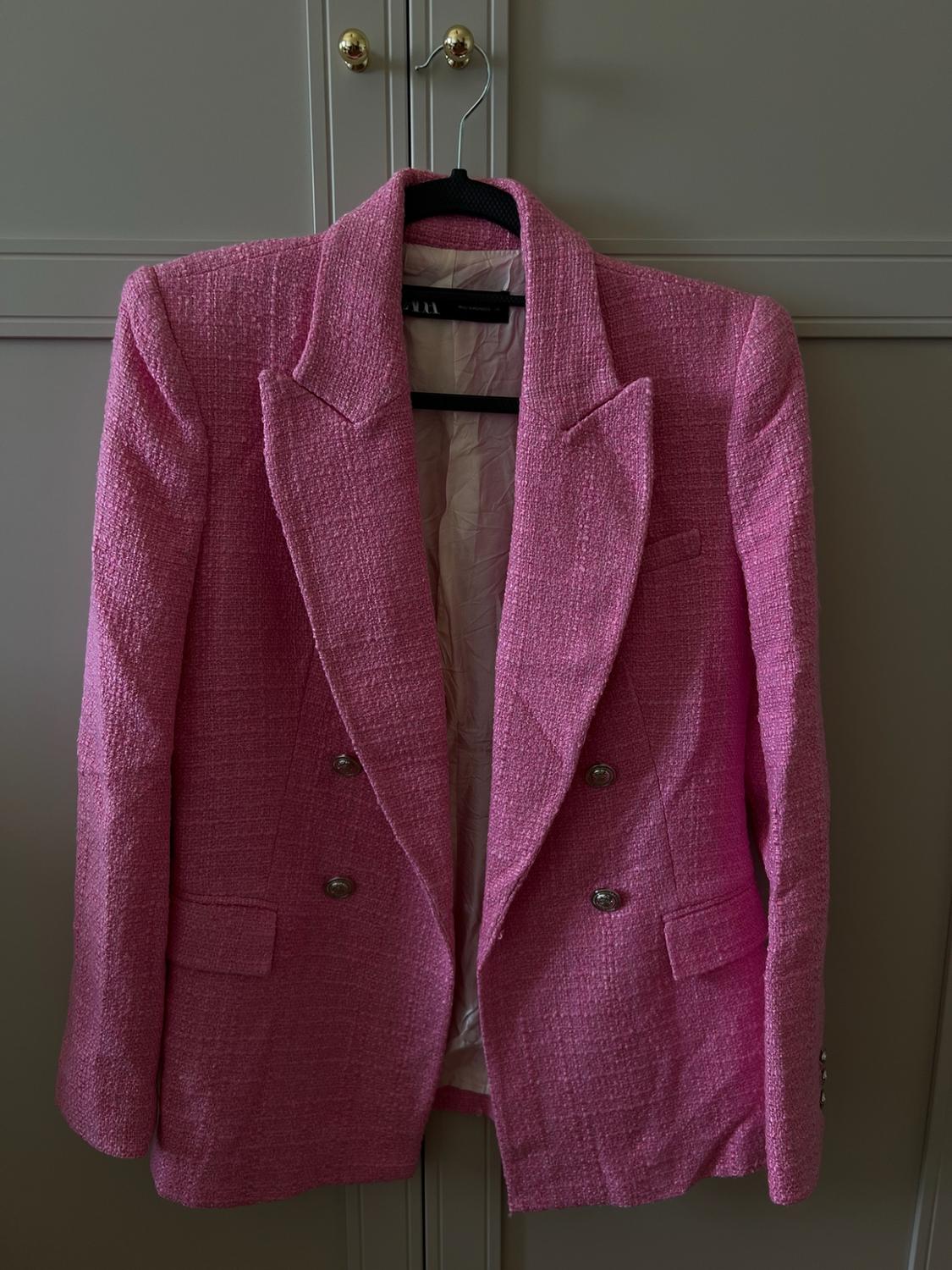 Textured pink double-breasted blazer with metallic buttons, hanging on a black hanger in front of a grey wardrobe. ZARA label.