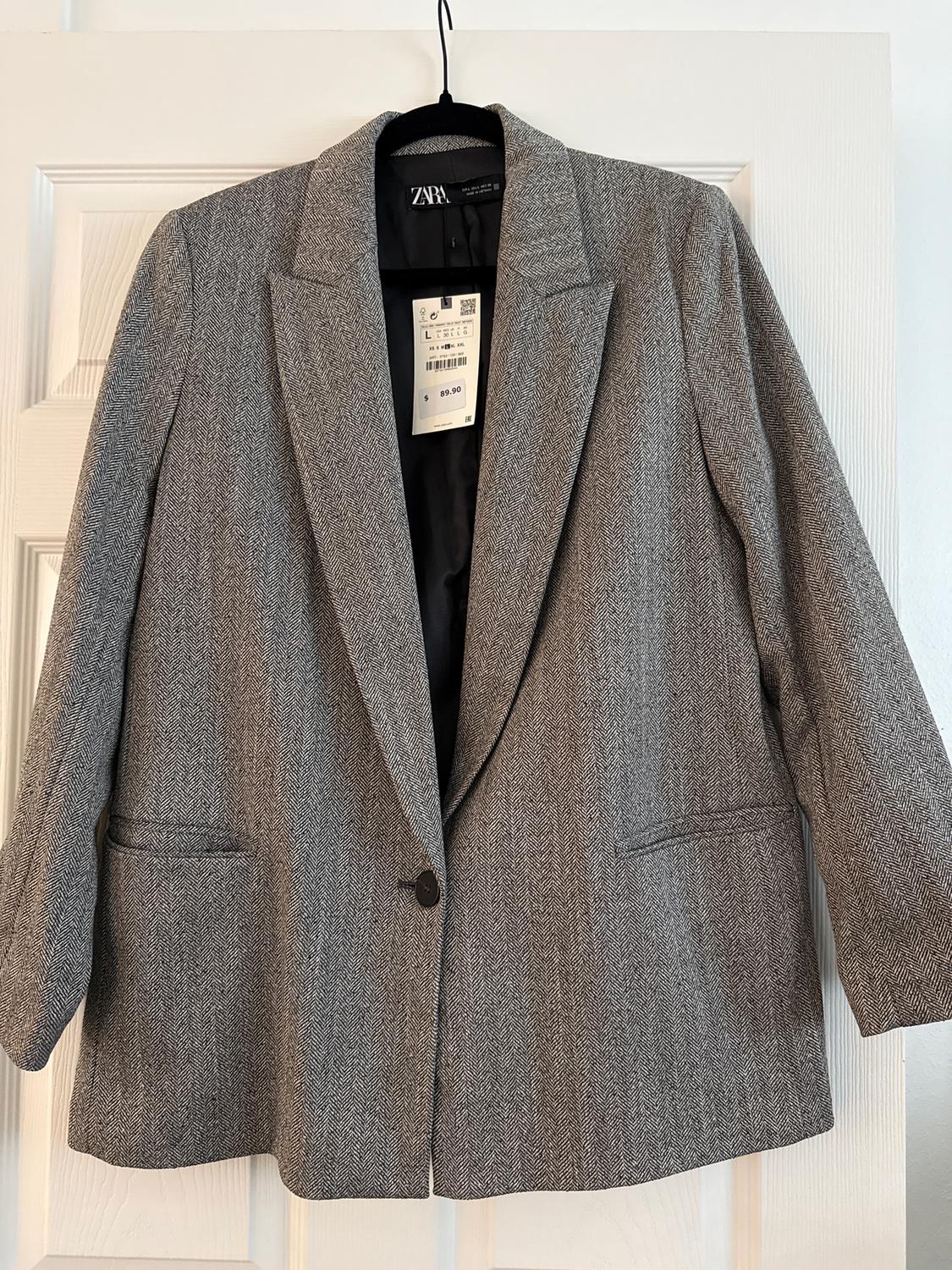 Grey herringbone jacket hanging on a white door. Visible tag with price of $89.90 and size L.