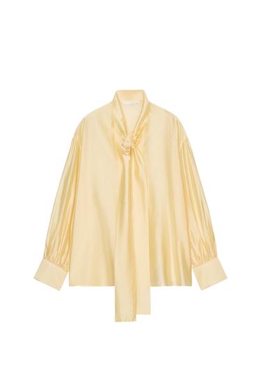 Front view of a yellow blouse with a neck tie, long puffed sleeves, and wide cuffs.