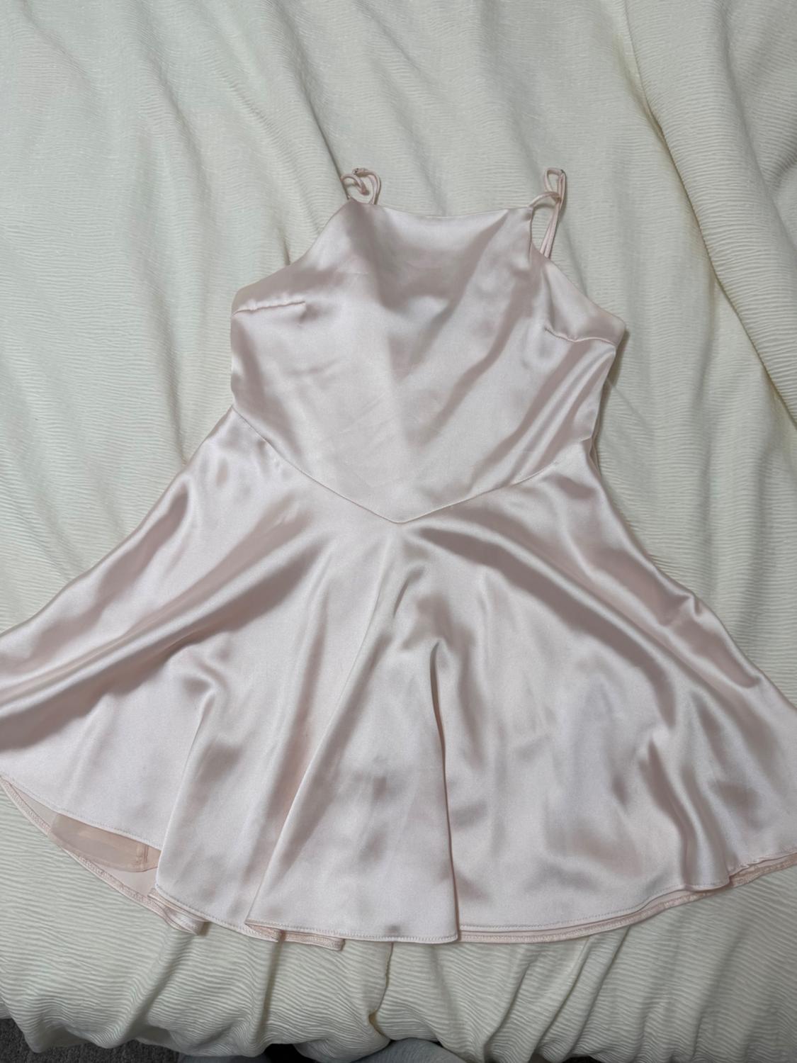 Light pink satin dress with spaghetti straps, spread out on a white bed. Soft, shiny fabric.