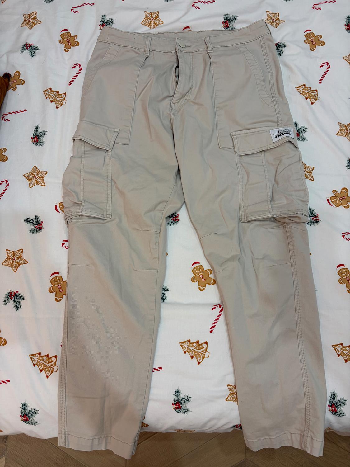 Beige cargo trousers on a bed with Christmas-themed sheets, such as candy canes and gingerbread biscuits.