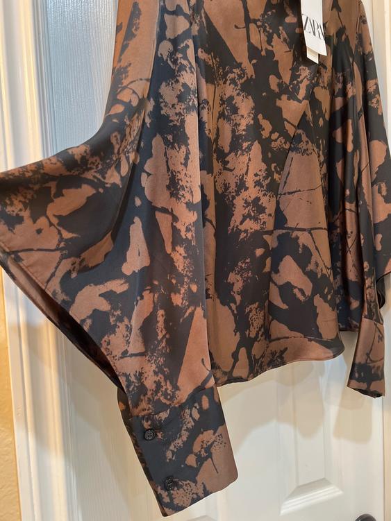 Long-sleeved shirt with an abstract print in brown and black tones, hanging on a white door. Visible tag with "ZARA" text.