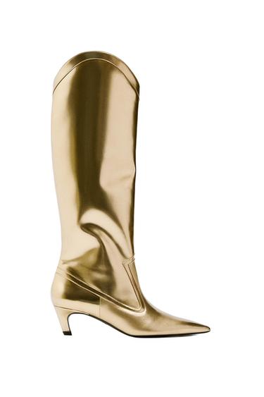 Metallic gold knee-high boot with a pointed toe, low heel and stitched detailing, on a white background.