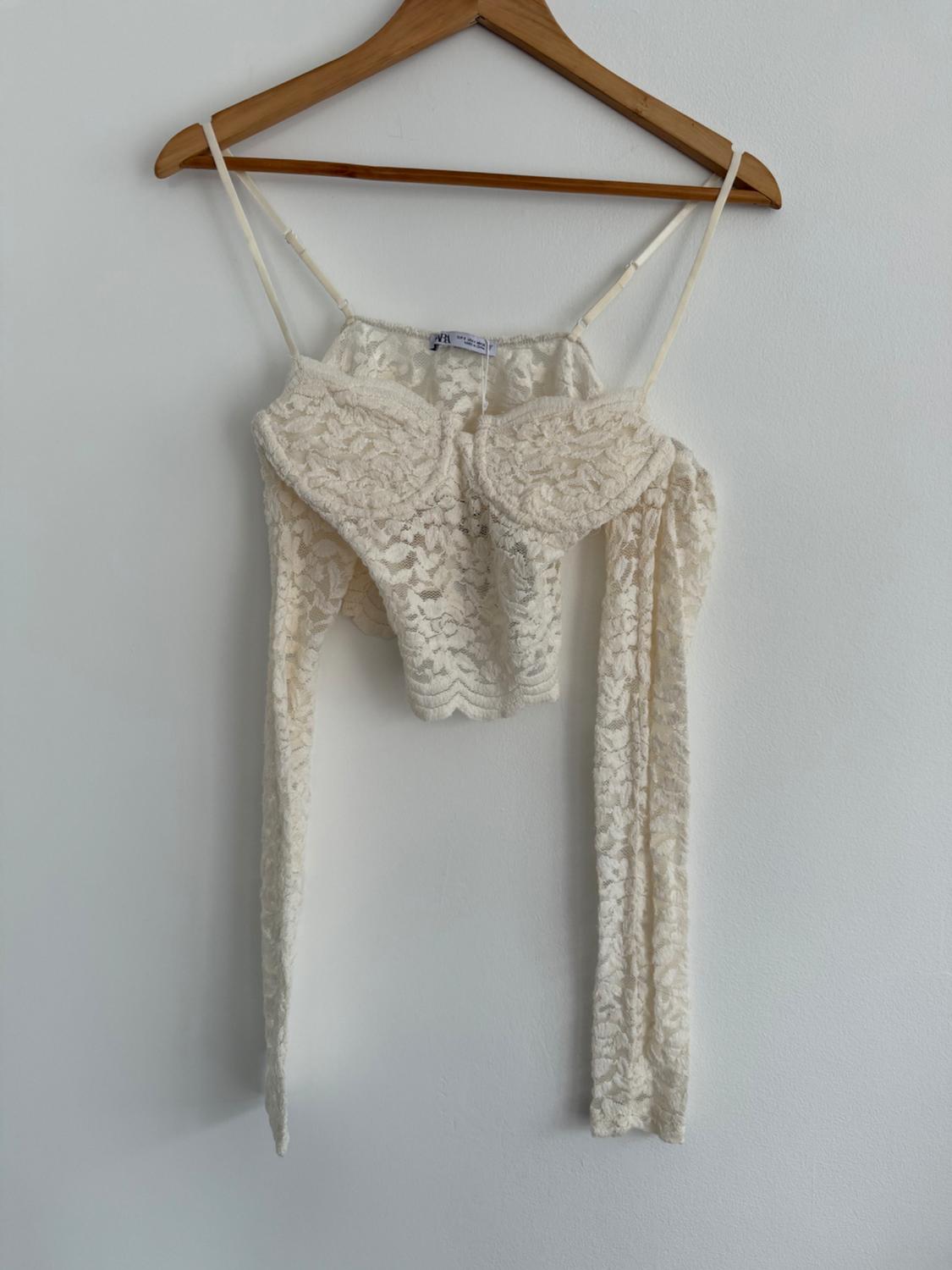 White lace camisole with spaghetti straps, hanging on a wooden hanger against a white wall.