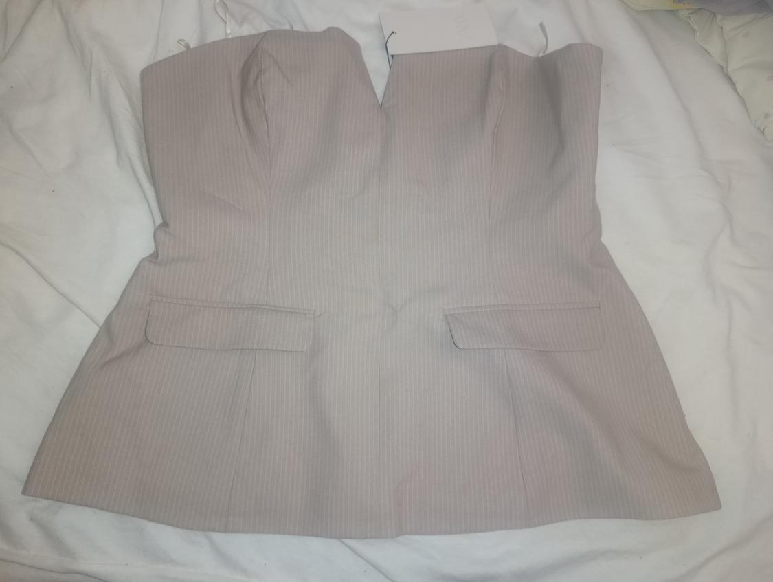 Tailored strapless light grey pinstripe top, with a V-neck and flap pockets, on a crumpled white sheet.