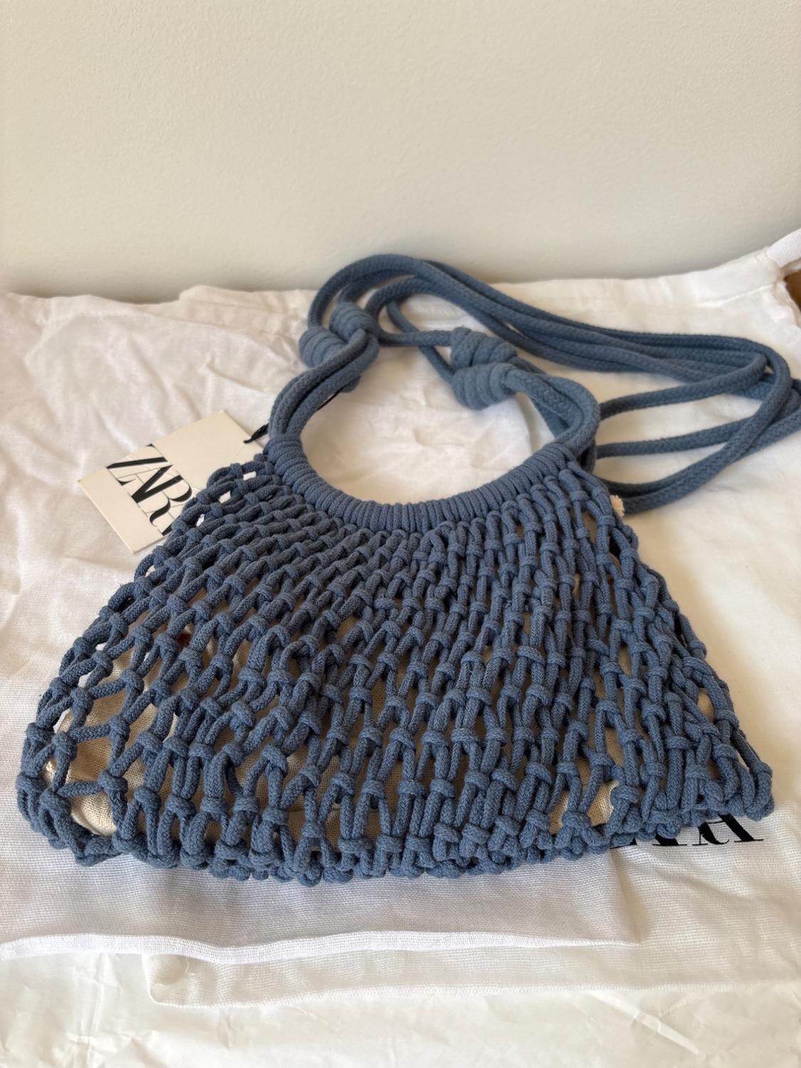 Blue mesh bag on white fabric with a visible tag that reads "ZARA". The design is a thick weave with long handles.