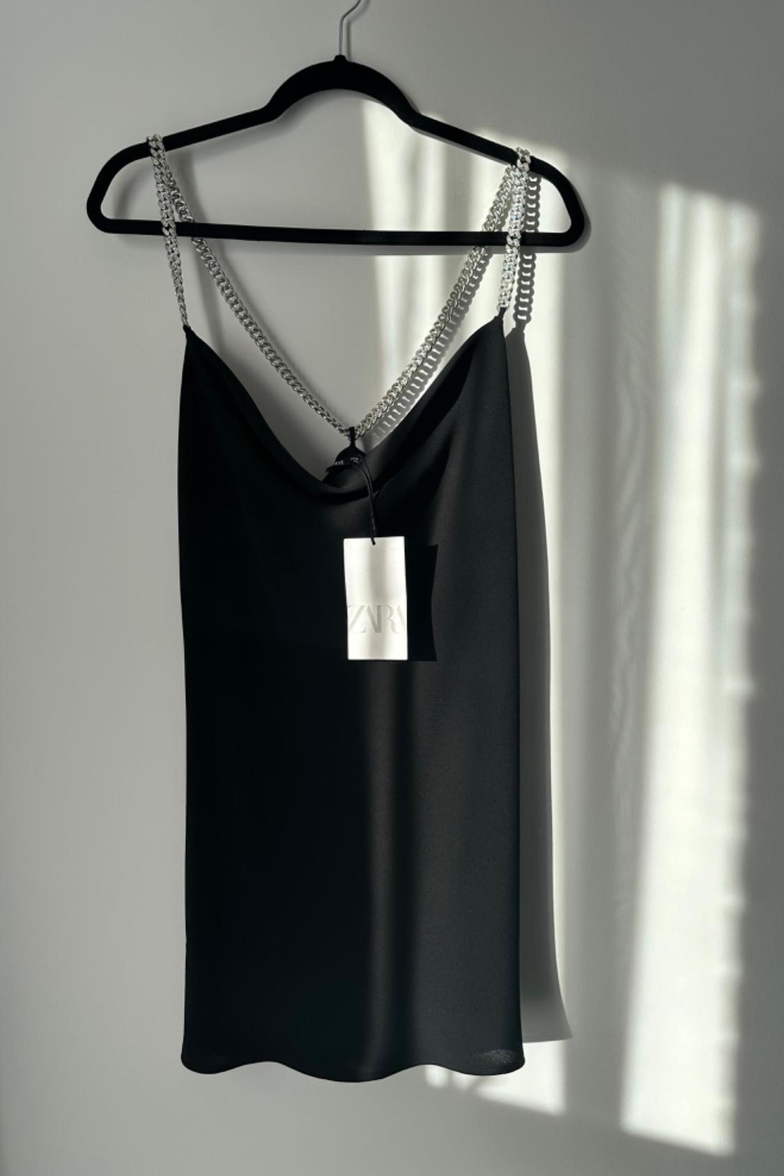 Front view of a black dress with silver chain straps on a hanger.