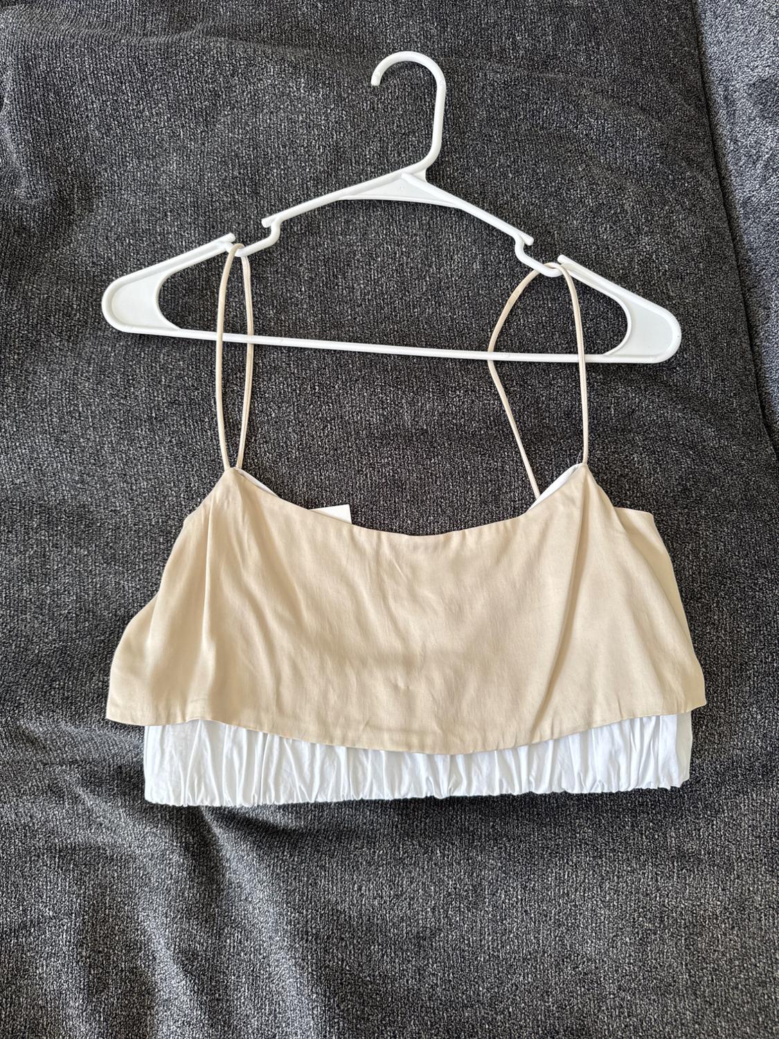 Beige and white tank top hanging on a white hanger over a gray fabric background.