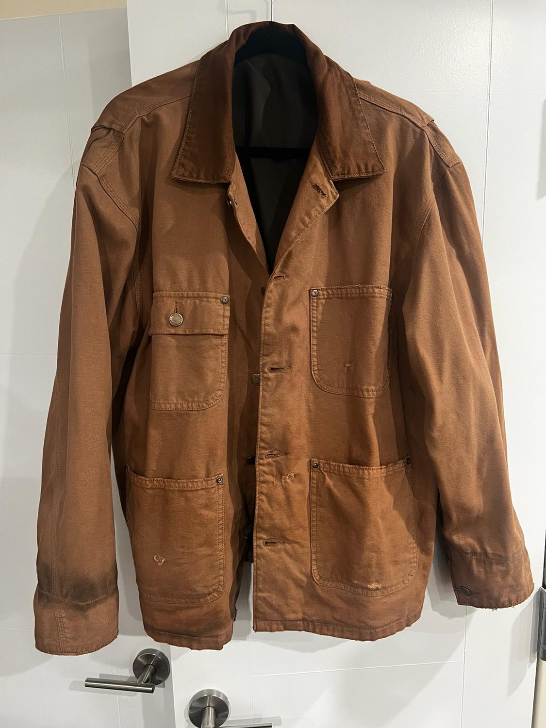Brown distressed-style jacket with a dark collar, buttons and four front pockets, hanging on a white door.