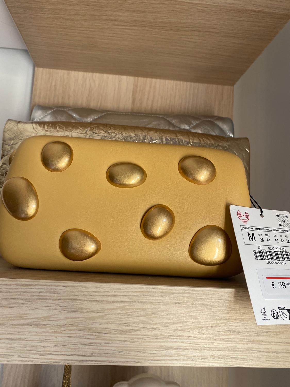 Yellow handbag with embossed gold details on a wooden shelf. Visible tag with price of €39.95.